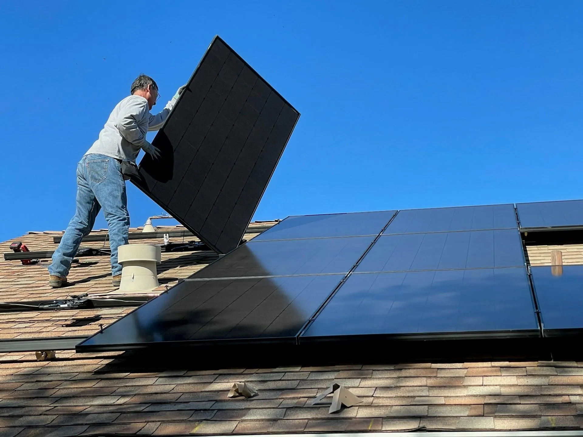 An installer positioning a solar panel beside an existing rooftop array